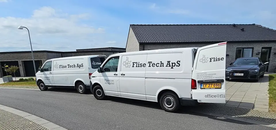 To hvide varebiler med Flise Tech ApS-logo holder foran et nybygget hus