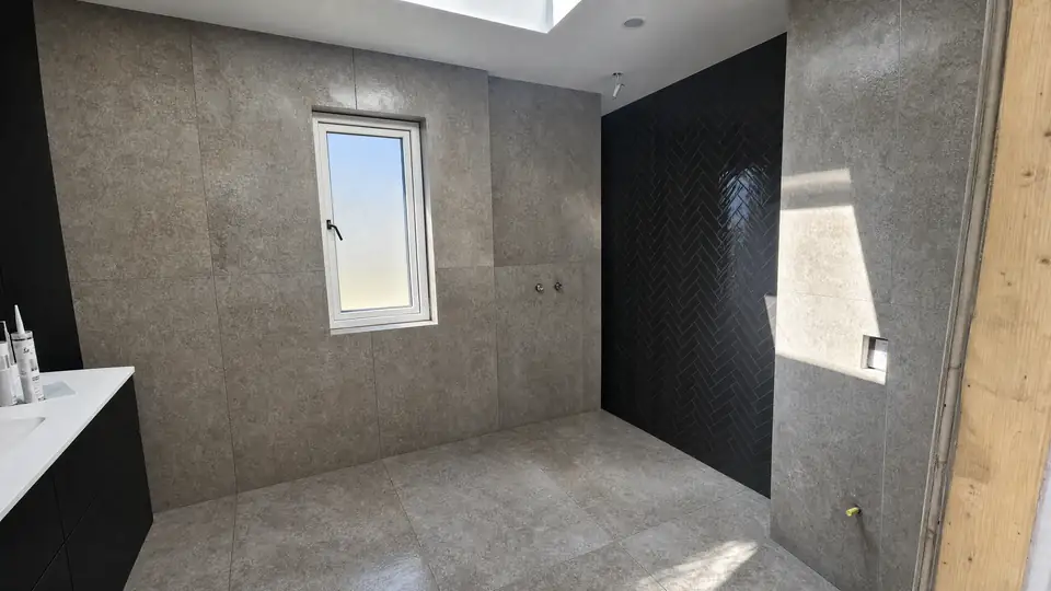 Færdigt badeværelse med store grå betonlook-fliser og en bruseniche beklædt med sorte blanke fliser i sildebensmønster